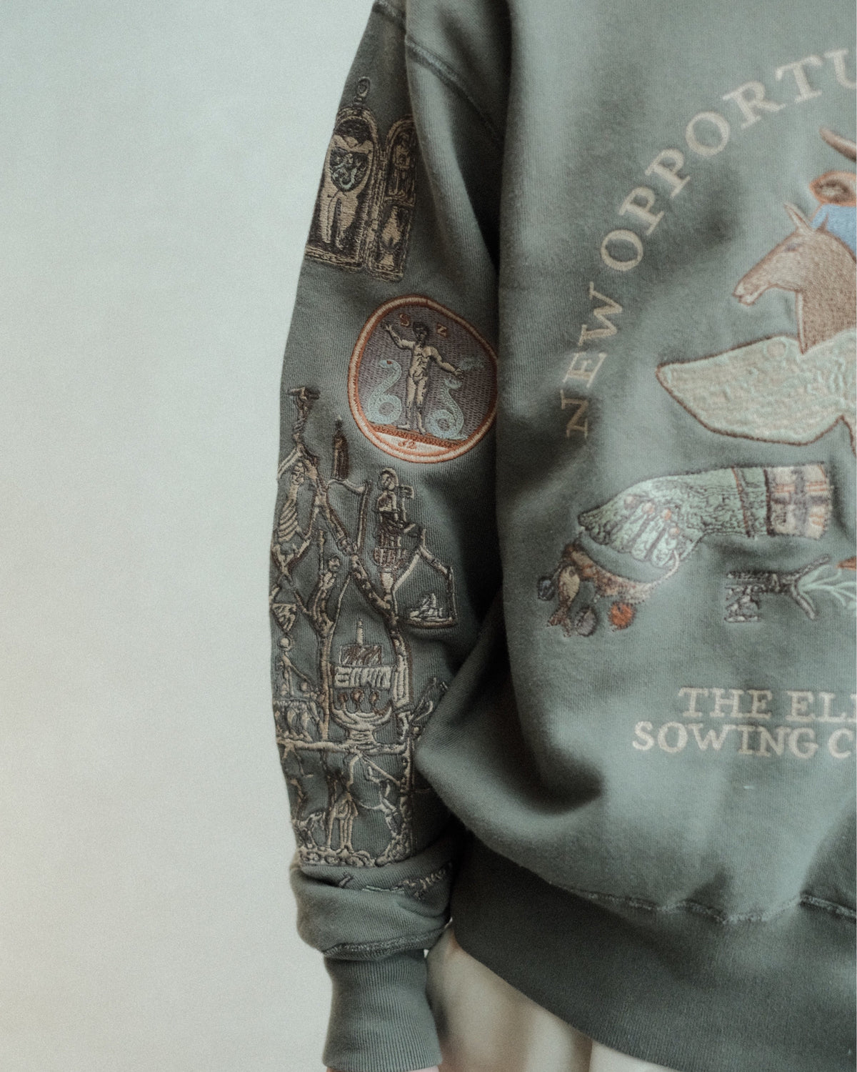 SAMUEL ZELIG Elder Crewneck Dark Sage EL-FW26-9-FT 反対側の袖の人物・円形モチーフ刺繍の詳細